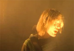 <i>Nirvana – Smell like teen spirit</i>” />Nel 1991 i Nirvana esplosero con <em>Nevermind</em> e Samuel  Bayer imprigionò l’icona di Kurt Cobain in una nuvola di polvere rossa, in un circo stanco e vecchio, già a pezzi nella serata di maggior successo. <em>Smells like teen spirit.</em><br />
Bayer è riuscito a raccontare una canzone, un gruppo, ciò che stava diventando simbolo del musicista geniale e disperato con <strong>intensa corporeità, con nuda intimità, faccia a faccia con il performer, con la sua essenza.</strong> Una tinta che Bayer ha perfezionato e raffinato, creando alcuni dei più importanti videoclip musicali degli anni ’90. Per poi sfociare nel capolavoro insieme ai Green Day con tutto <em><A href=